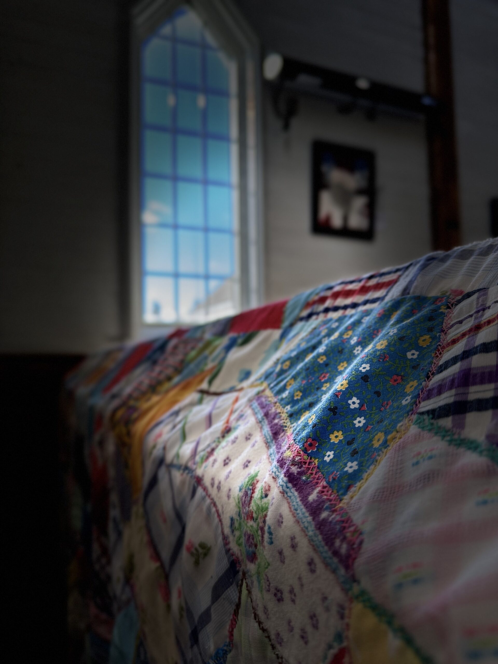 a patchwork quilt draped over a church pew with light coming in a window and falling on it