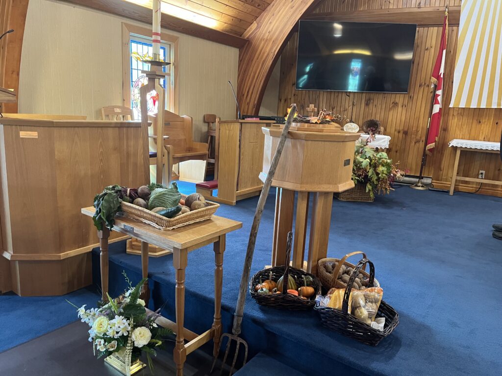 Church interior with harvest decorations including vegetables, baskets, and a pitchfork.