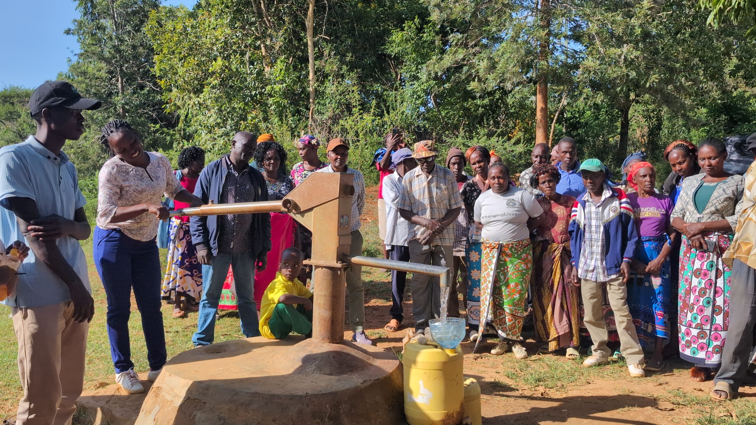 Group of people standing by a water pump outdoors.