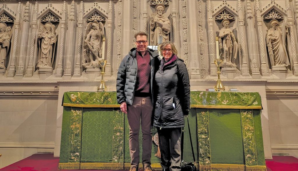 Man and woman standing in front of an altar with carved figures.
