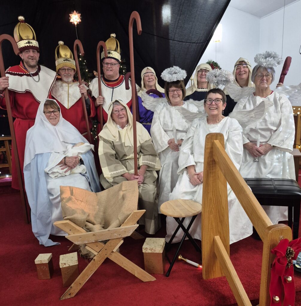 A group pose of the nativity play cast in costume, including the three kings, Mary, Joseph, and angels.