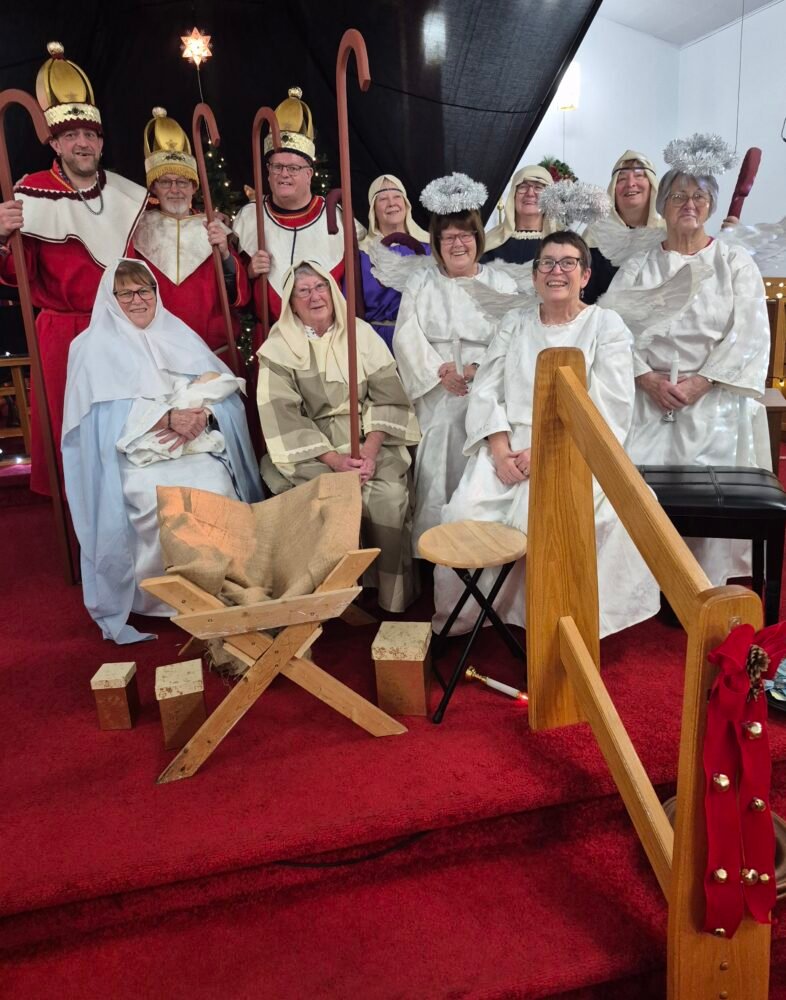 A group pose of the nativity play cast in costume, including the three kings, Mary, Joseph, and angels.