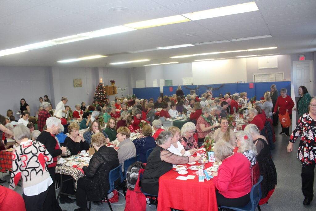 a group of people havign tea in a church hall that is decorated with red table cloths