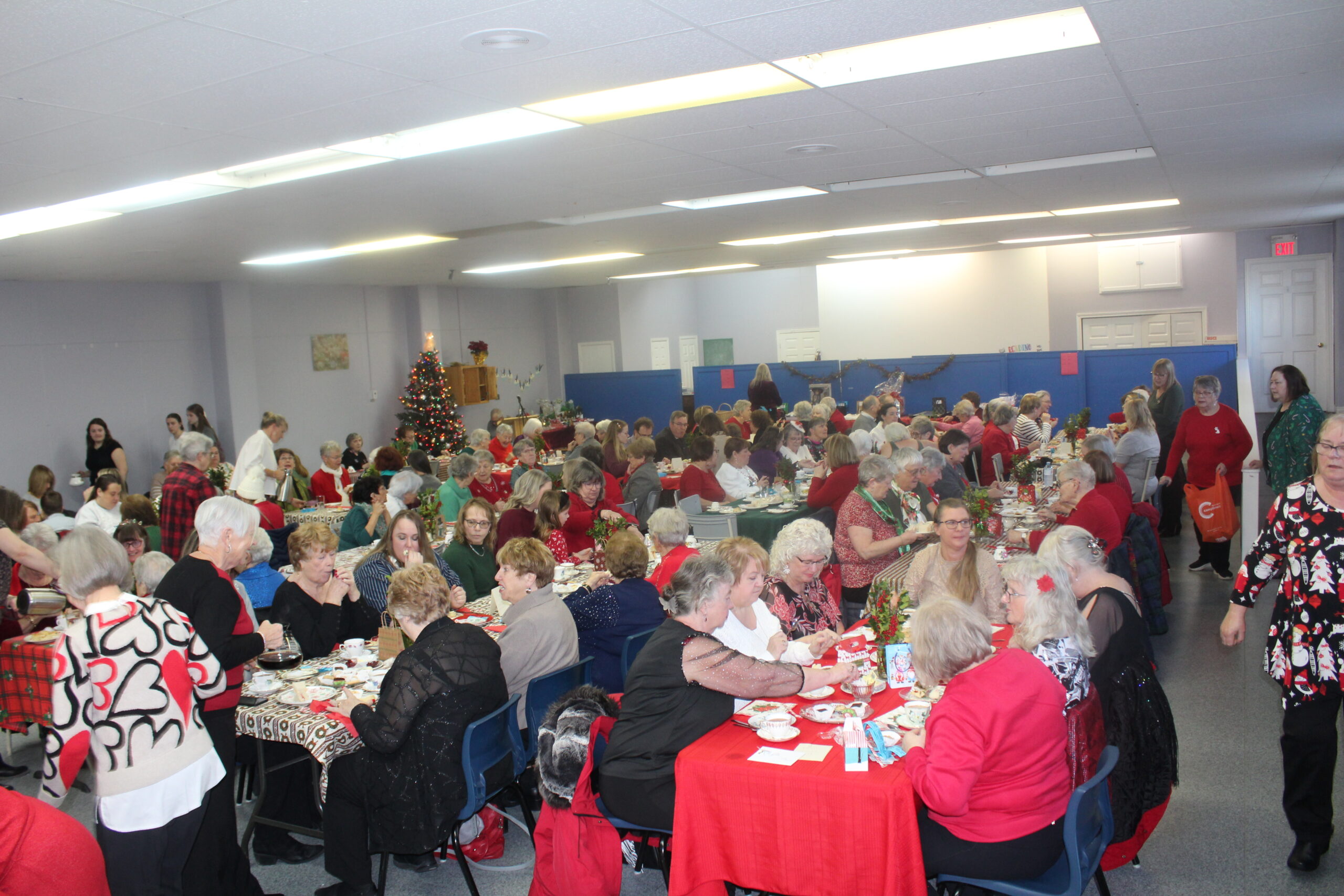 a group of people havign tea in a church hall that is decorated with red table cloths