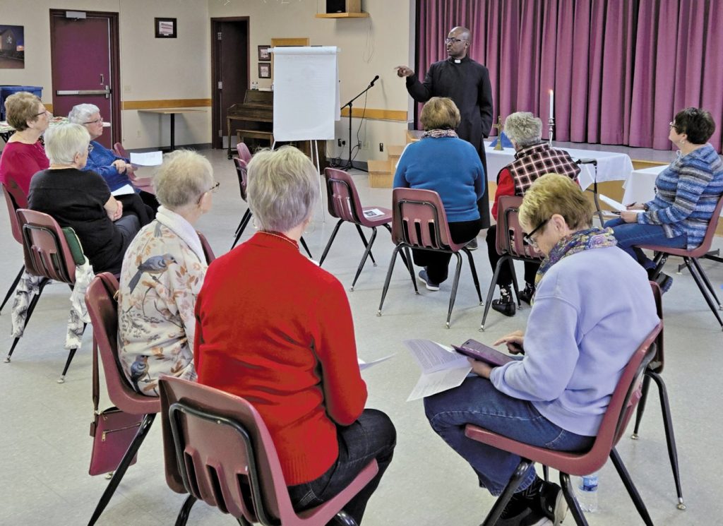 Group of women seated in a circle listening to a man speaking.