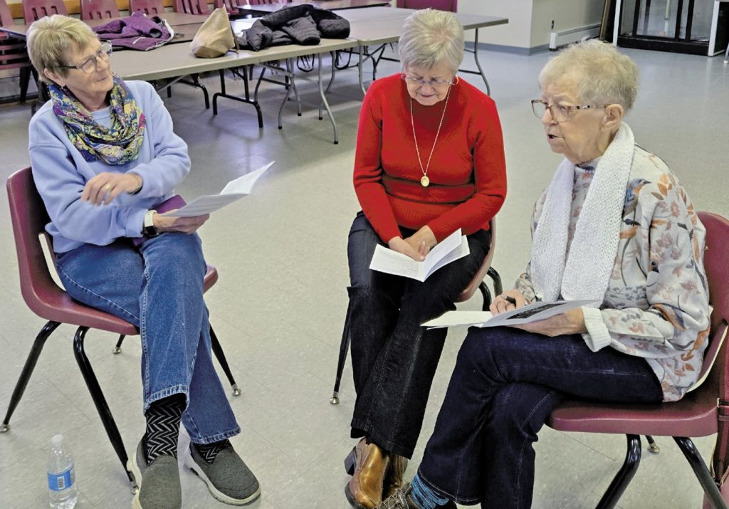 Three women seated in a circle reviewing documents.