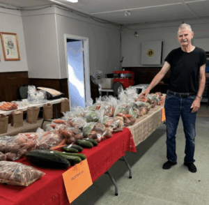 A man standing next to a long table filled with bags of fresh vegetables.