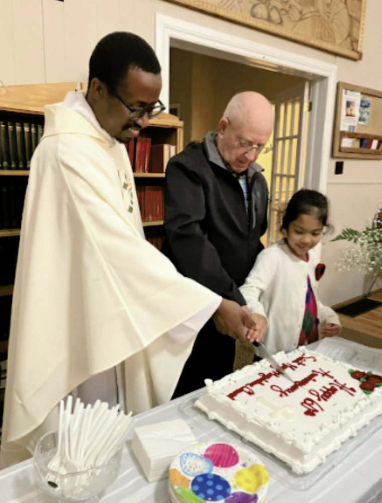 Three people smiling while cutting a celebratory sheet cake together.