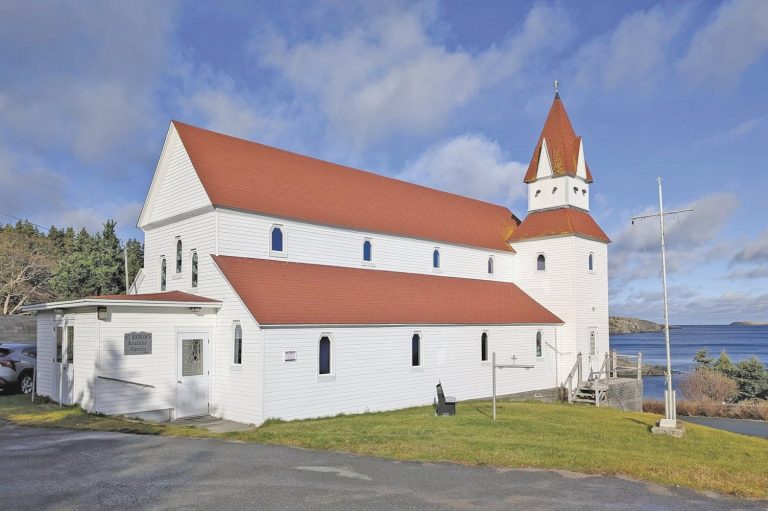 Exterior view of a white church with a red roof situated near a body of water.