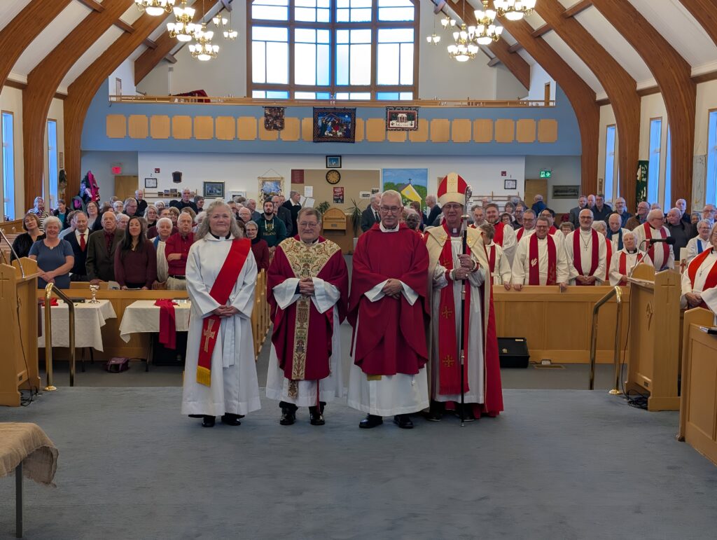 A large group of clergy and a bishop stand at the front of a sanctuary with a seated congregation behind them.