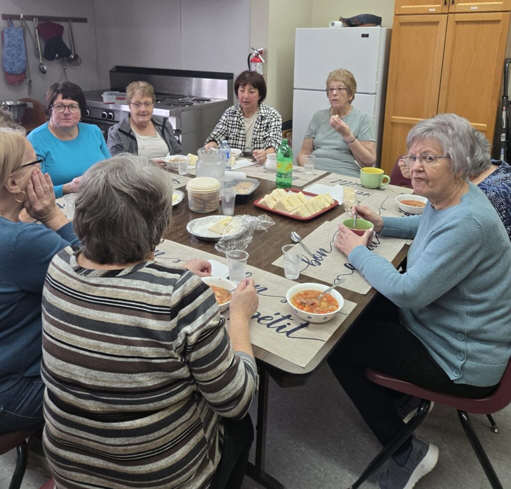 A large group of people seated at long tables enjoying a meal in a community hall.