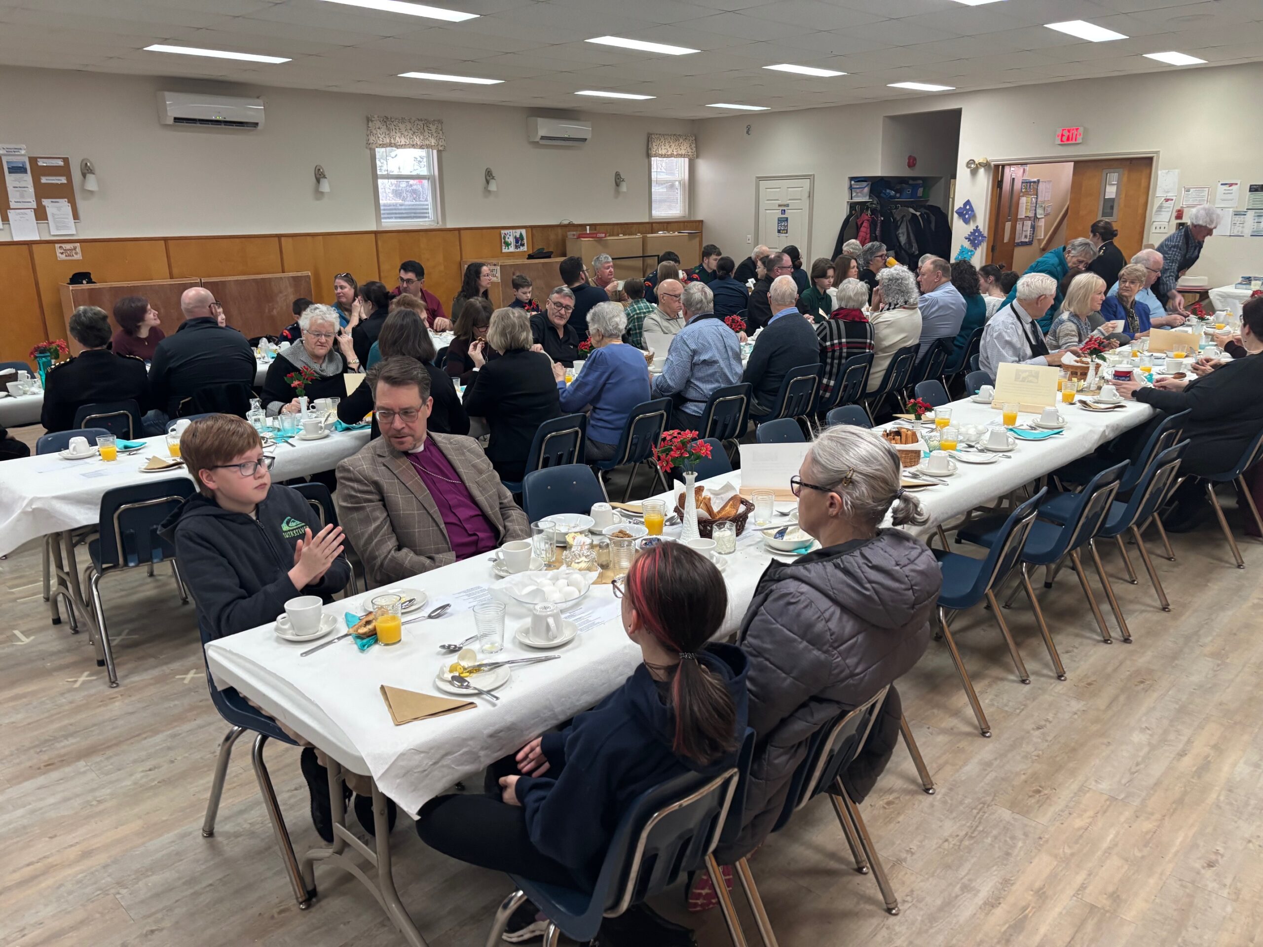 A large group of people seated at long tables enjoying a meal in a community hall.