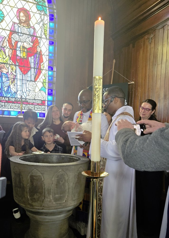 A group of people gather around a stone baptismal font in a church during a ceremony.