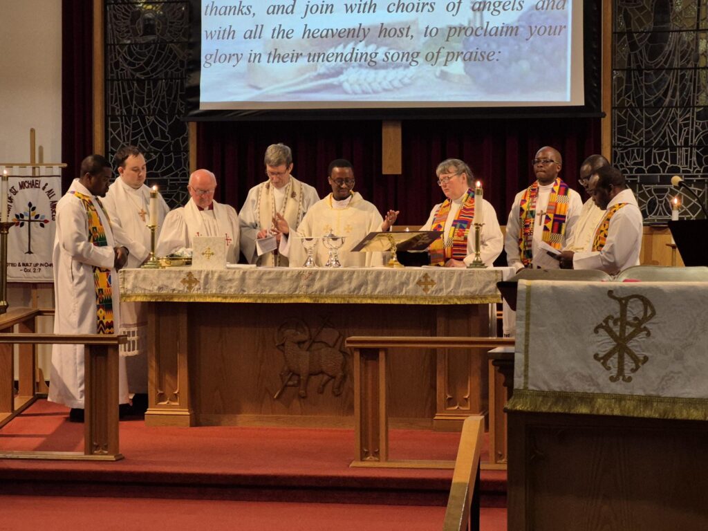 a group of clergy standing behind a wooden altar, dresssed in white vestments with colourful stoles