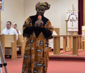 a woman in traditional African clothing singing into a microphone at the front of a church