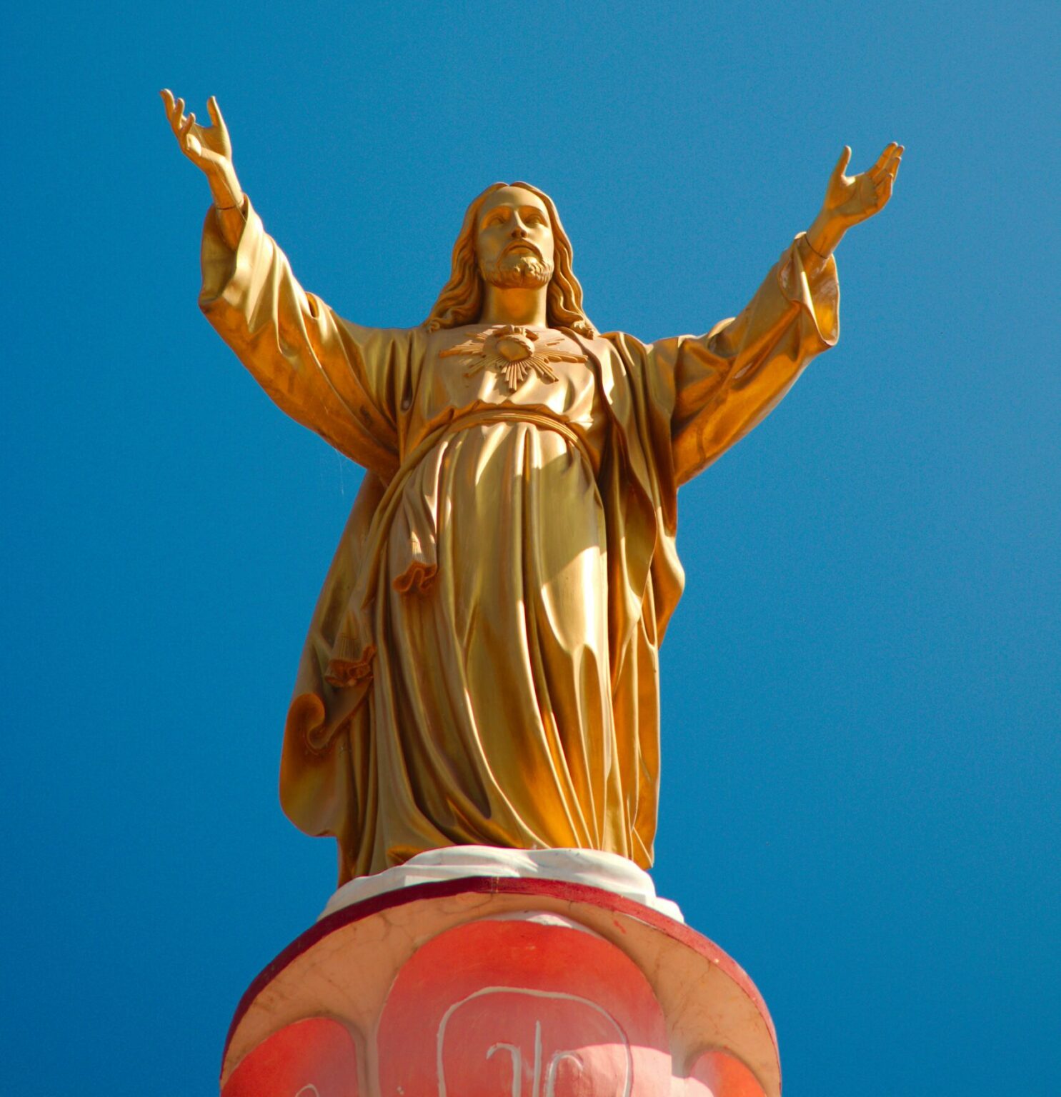 a statue of Jesus with his arms ourstretched in blessing against a cloudless blue sky