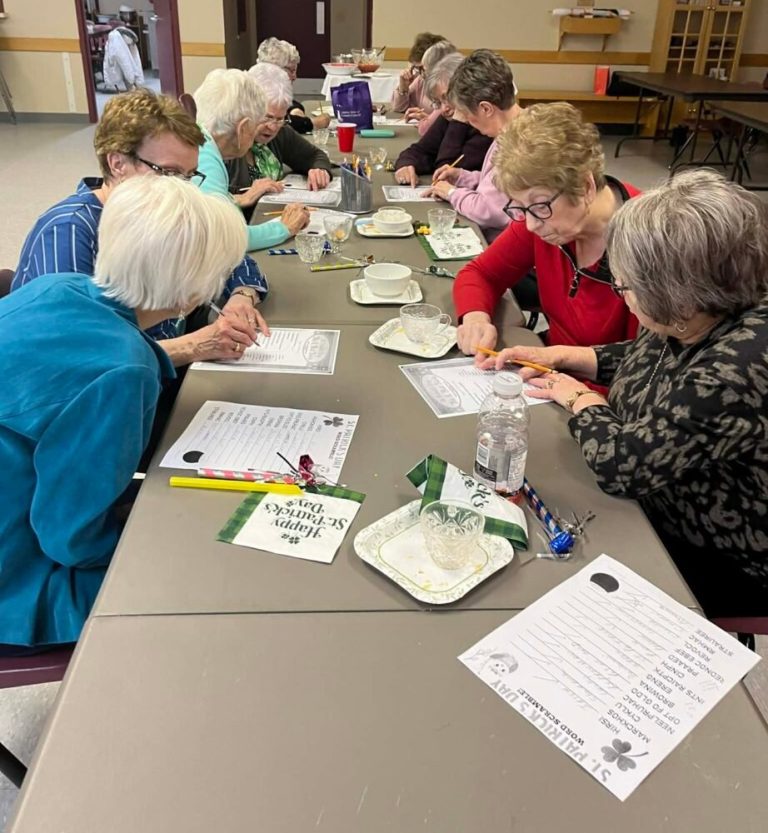 women work together on word puzzles on a long table in a church hall
