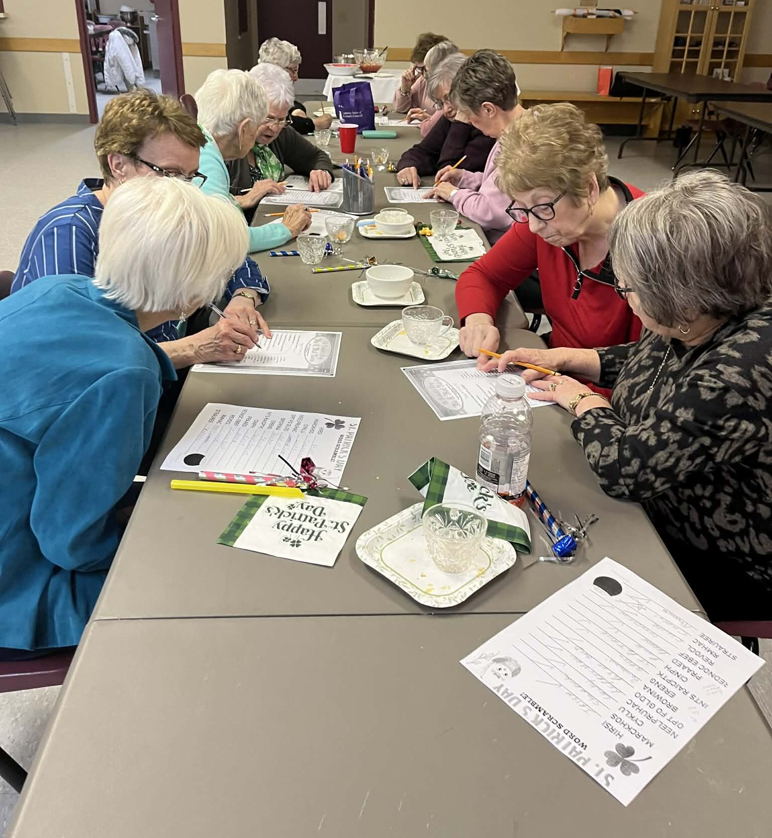 women work together on word puzzles on a long table in a church hall