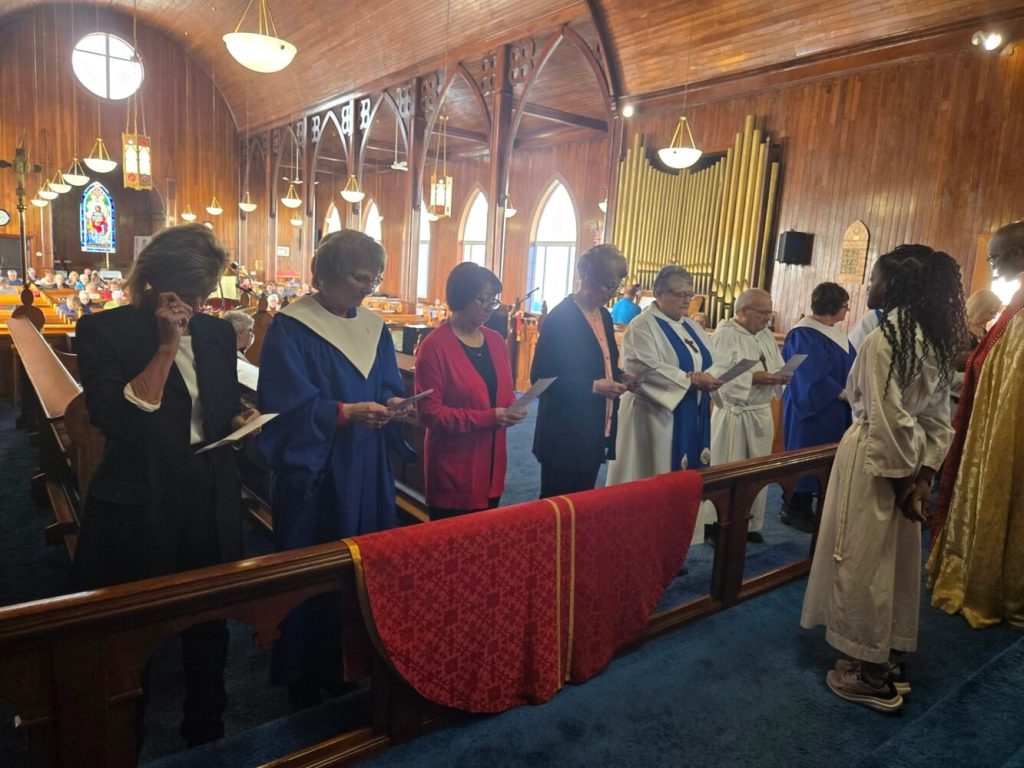 a group of people standing behind an altar rail that has a red chasuable resting on it.