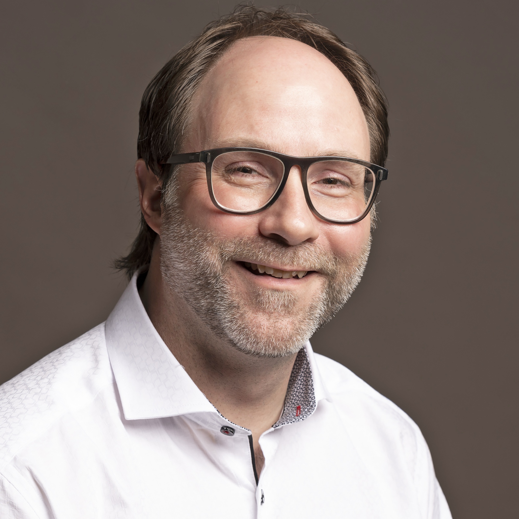 a man with a short beard and glasses in a white shirt smiles at the camera