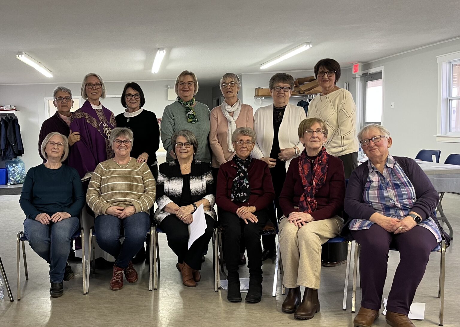 A group of thirteen women posing for a photo in a bright room.