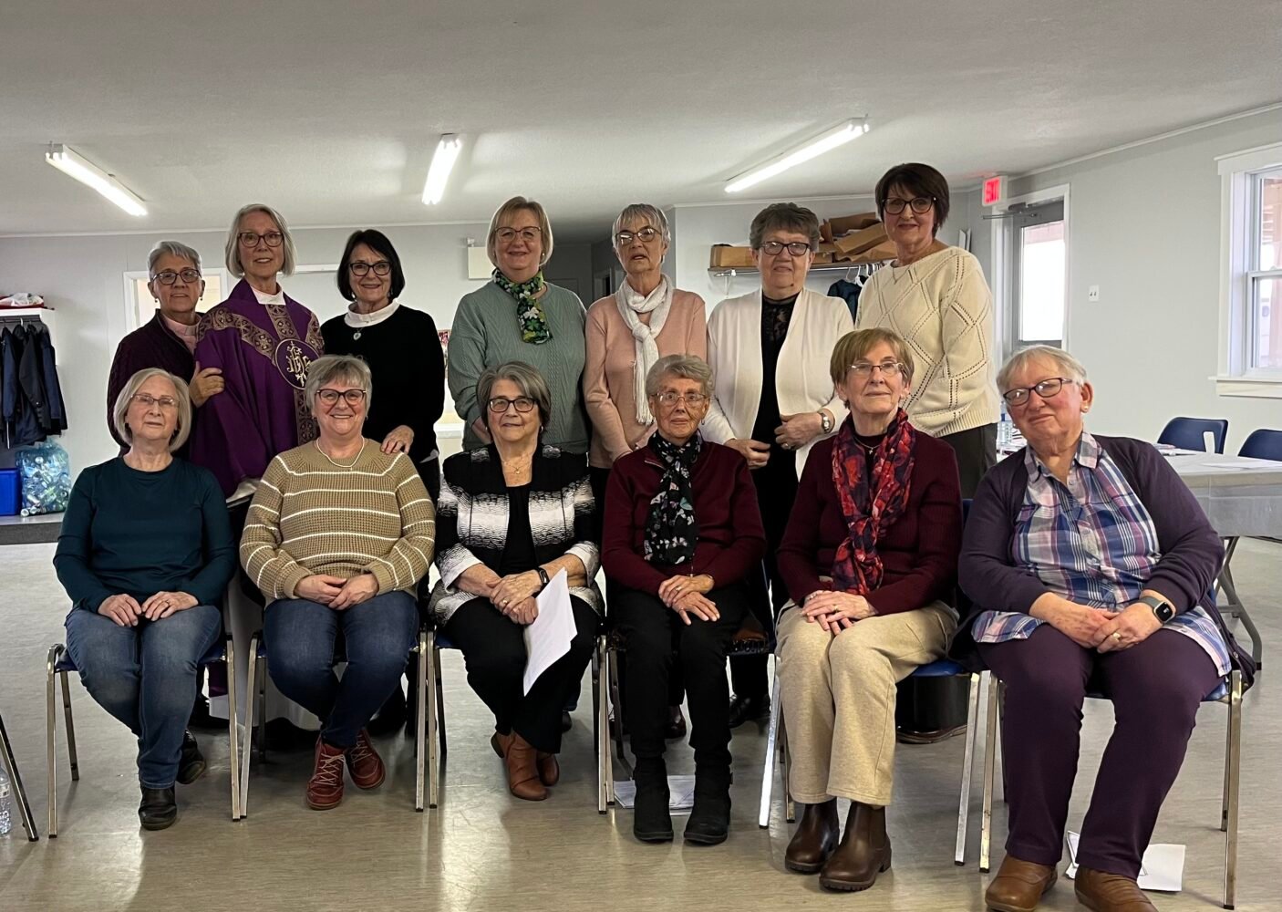 A group of thirteen women posing for a photo in a bright room.