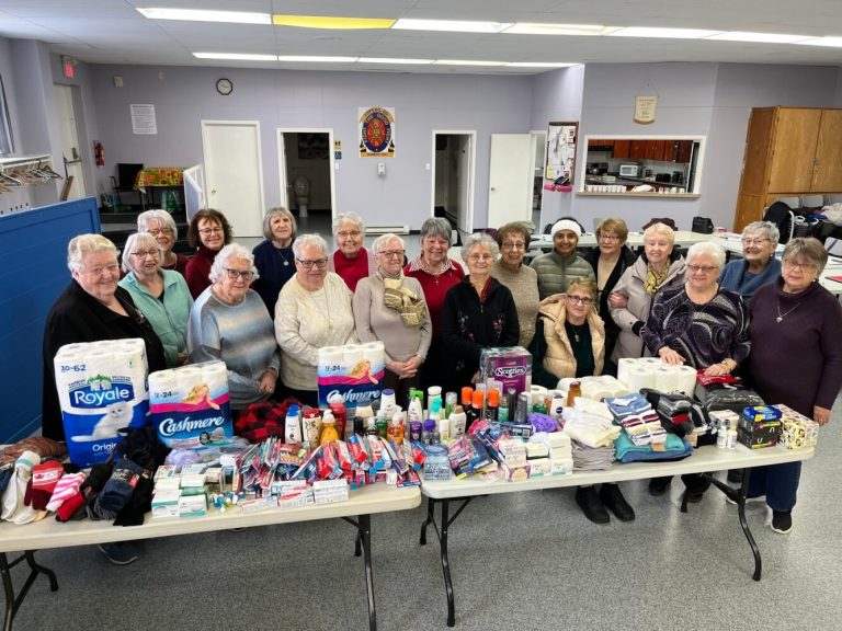 A group posing behind tables filled with donated toiletries and household goods in a community hall.