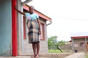 A pregnant woman standing in a doorway wearing a traditional blanket.