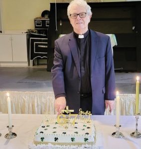a man dressed as a priest cuts a cake on a table that also has many candles on it.