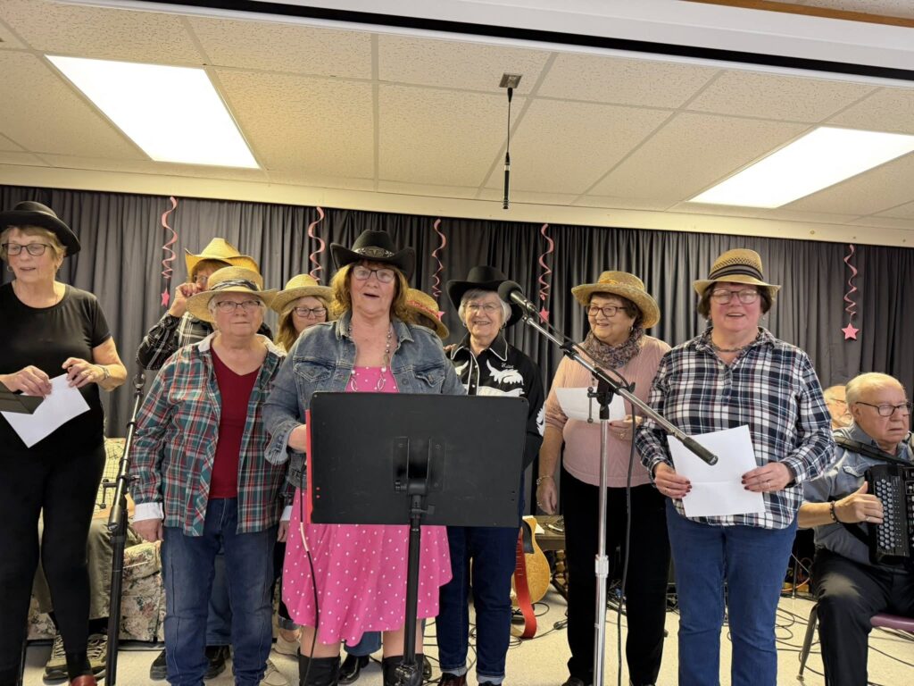 A group of people wearing cowboy hats and plaid shirts singing together on a stage.