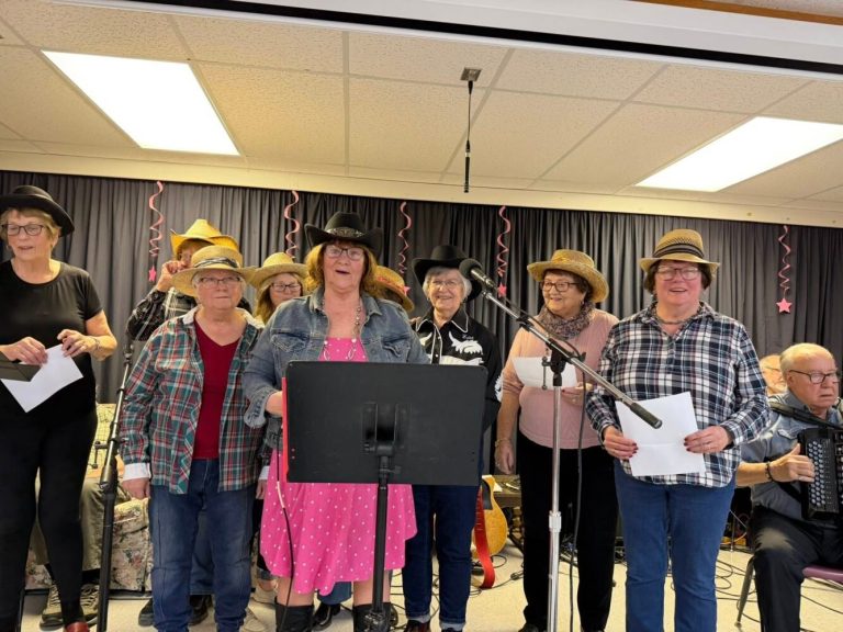 A group of people wearing cowboy hats and plaid shirts singing together on a stage.
