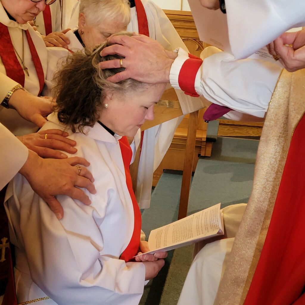 a woman kneels and has hands placed on her head