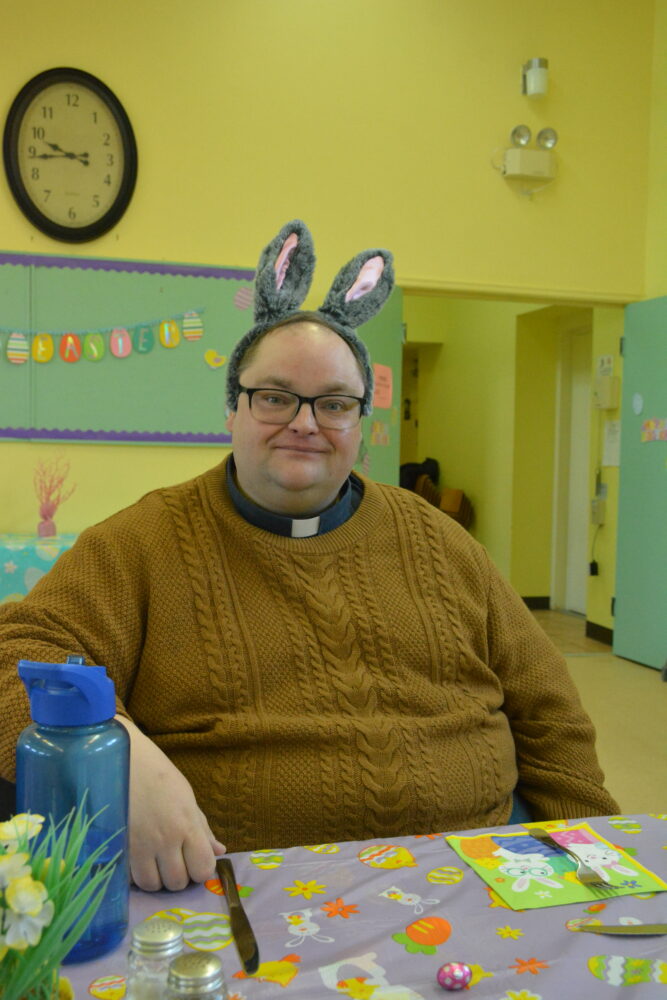 A man wearing gray bunny ears and a brown sweater sits at a decorated table.