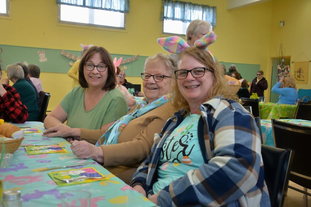 Close-up of three women smiling, one wearing colorful bunny ears.