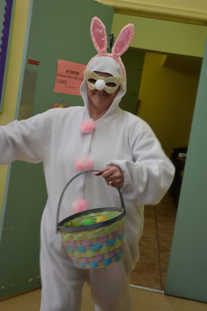 A person in a full white bunny costume and a sparkly mask carries an Easter basket.