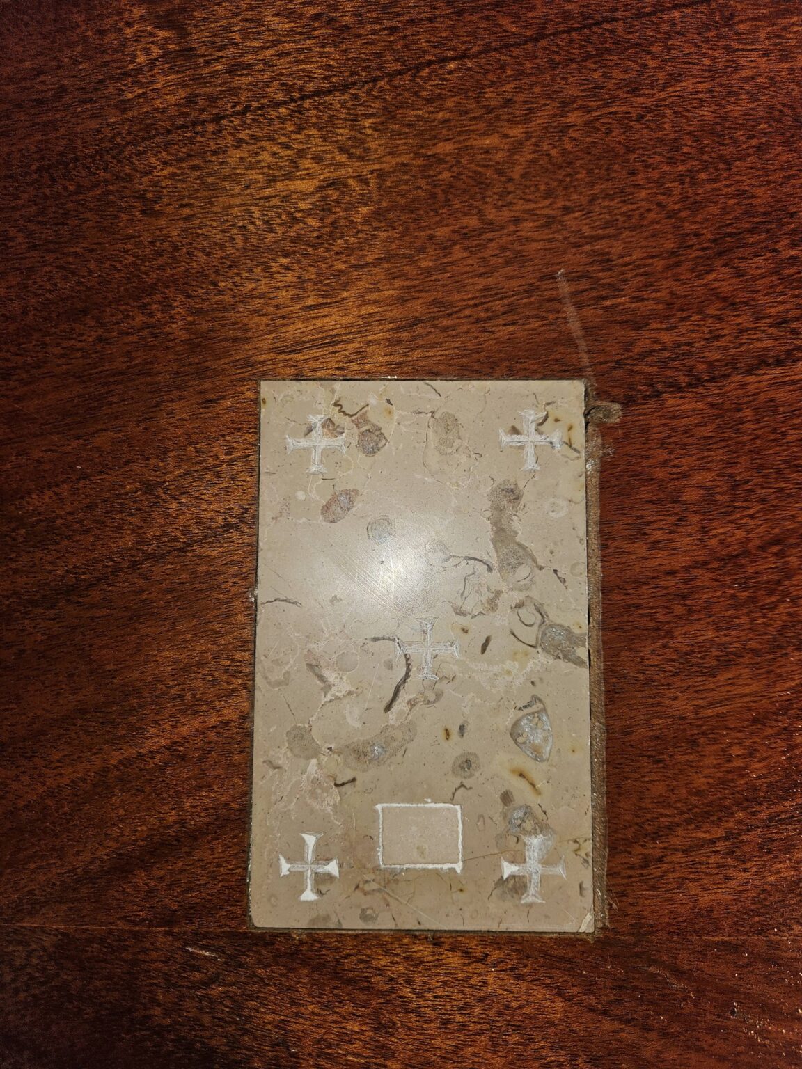 A rectangular stone slab with five small white crosses etched into it, resting on a dark wood surface.