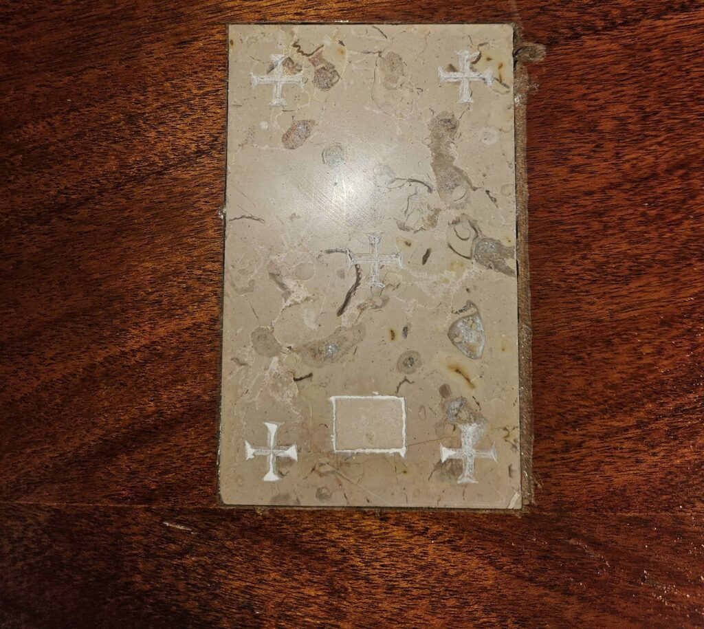 A rectangular stone slab with five small white crosses etched into it, resting on a dark wood surface.