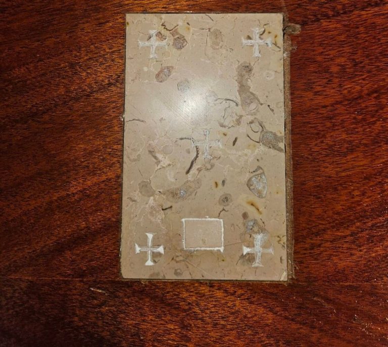 A rectangular stone slab with five small white crosses etched into it, resting on a dark wood surface.