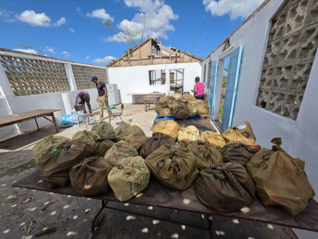 Dozens of filled yellow and brown bags sit on tables inside a roofless, damaged building being used for aid distribution.