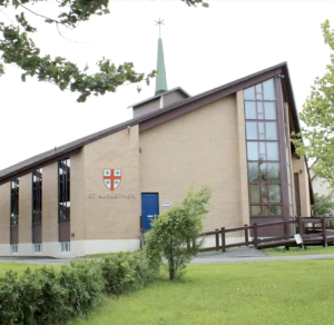 
Modern tan brick church with a green steeple, tall stained-glass windows, and the name "St. Augustine's" below a red and white crest.