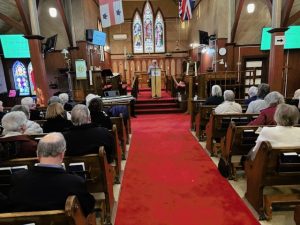 congregation in a wooden church with red carpet listening to a man speaking at the front