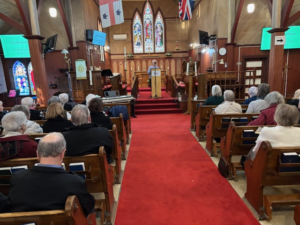congregation in a wooden church with red carpet listening to a man speaking at the front
