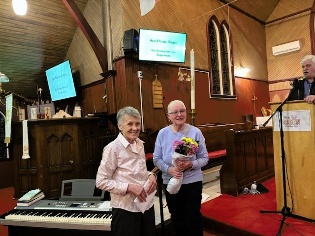 two older women: one in blue, holding flowers, and one in pink