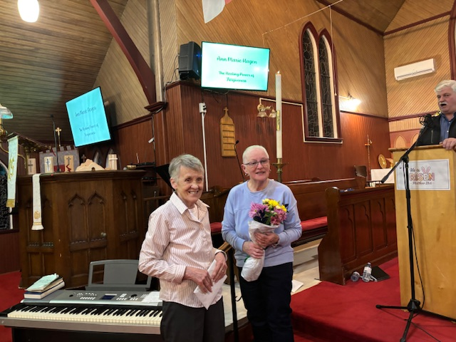 two older women: one in blue, holding flowers, and one in pink