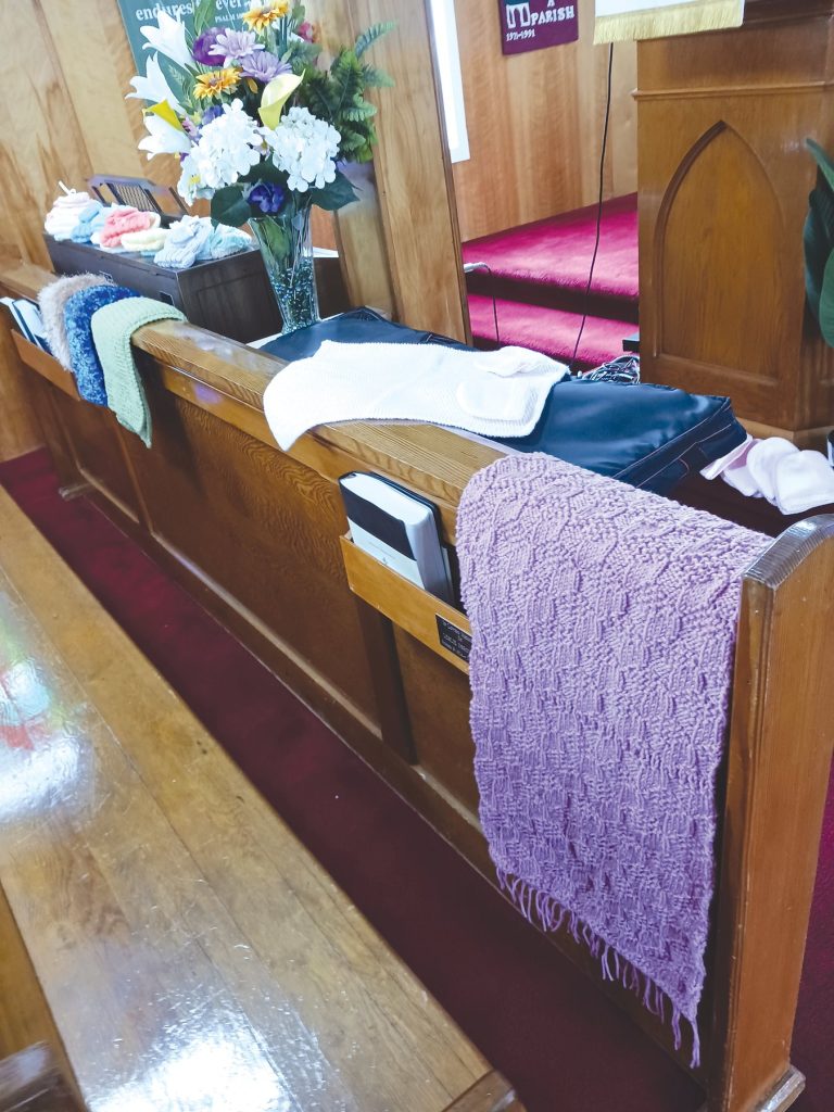 A purple knitted scarf with fringe hanging over a wooden church pew.