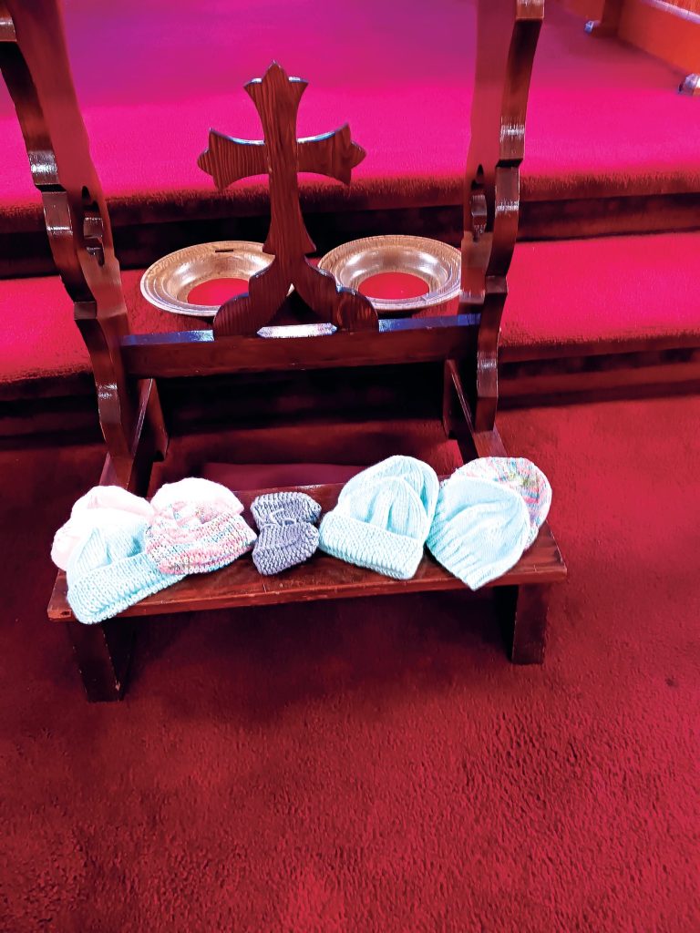 Small knitted hats displayed on a wooden stand beneath a cross.