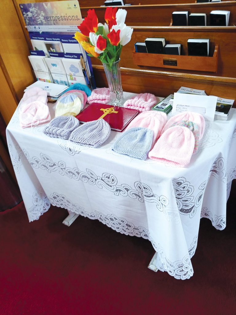 Knitted hats and a flower vase on a table covered with a white tablecloth.