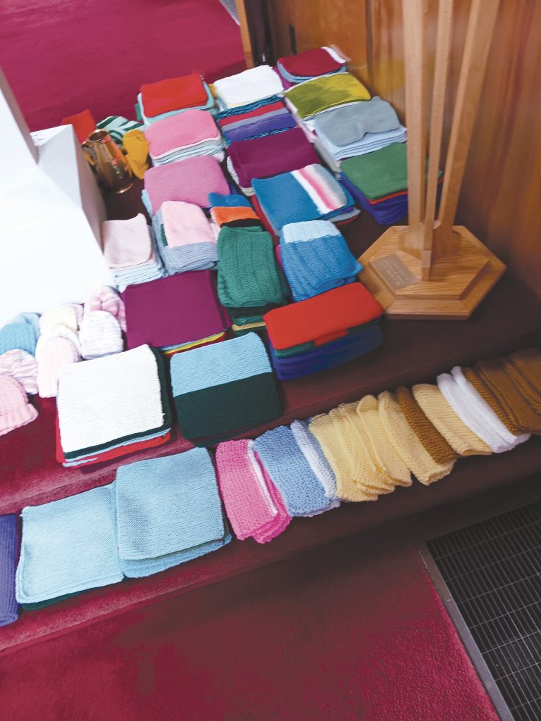 Stacks of colourful knitted washcloths and items arranged on steps by the base of a wooden candle holder