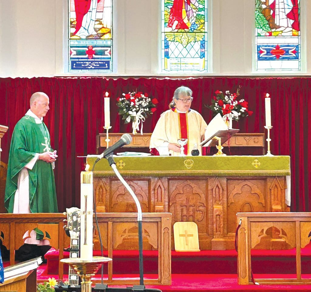 a preist stands behind an alrat with at white chasuable on. To her right is another priest in a green chasuable