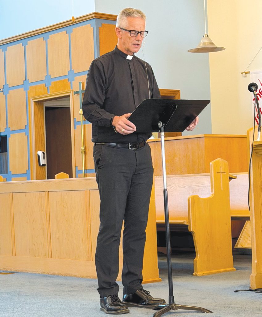 a priest speaks from a folding lectern at the front of a church